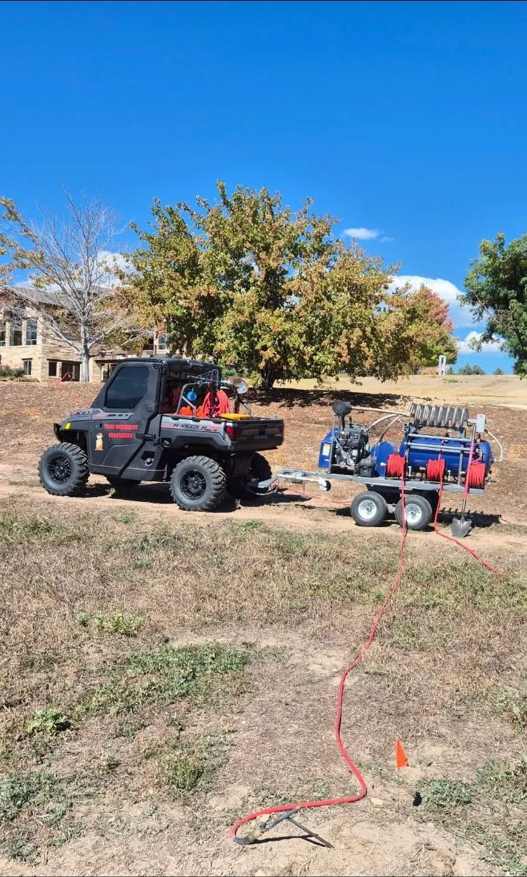 The Rodent Ranger’s new rig on a job: a black Polaris Ranger and the blue PERC trailer, a red hose run out to an orange marker flag