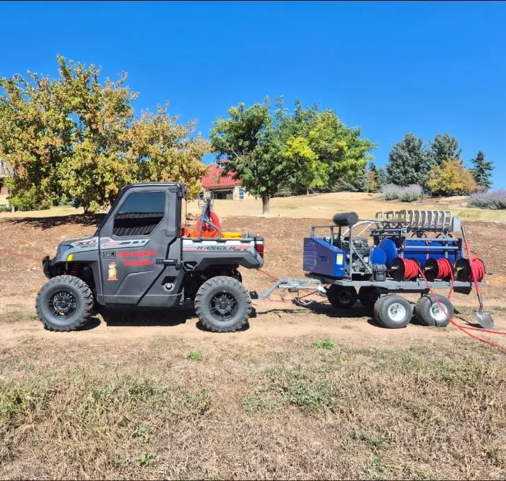 Side view of the new rig: a black Polaris Ranger hitched to the PERC trailer with its blue tank and red hose reels